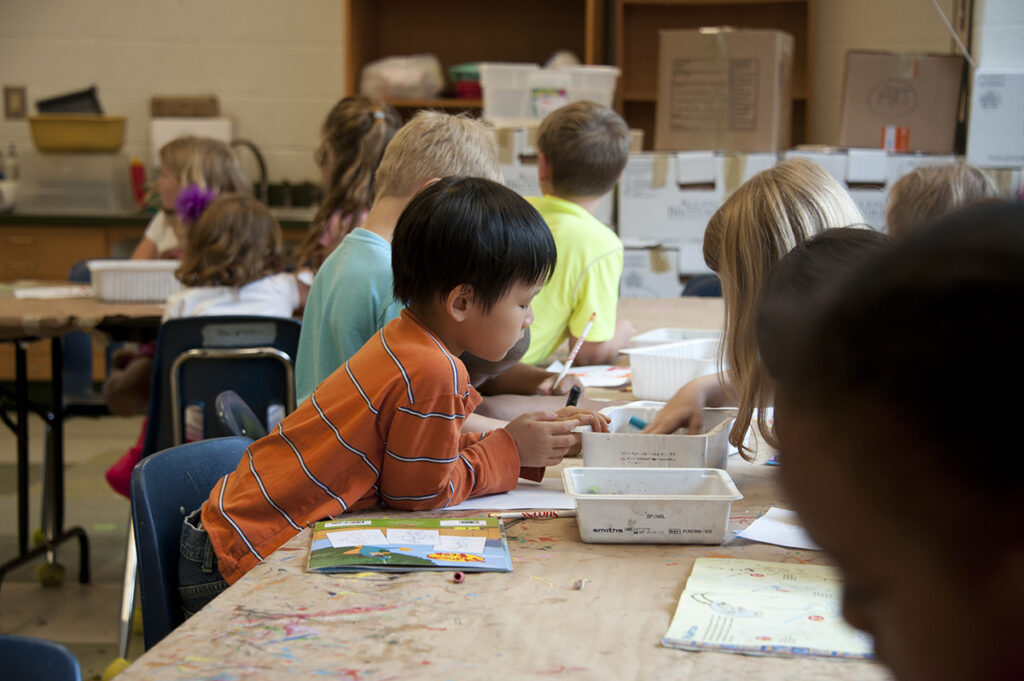 Young boy coloring with other students in a classroom